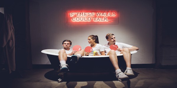 Three people in tennis outfits siting in a drained, non functioning bathtub holding pingpong paddles 