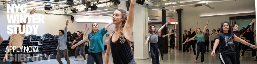 Many dancers fill a large studio reaching into the air.