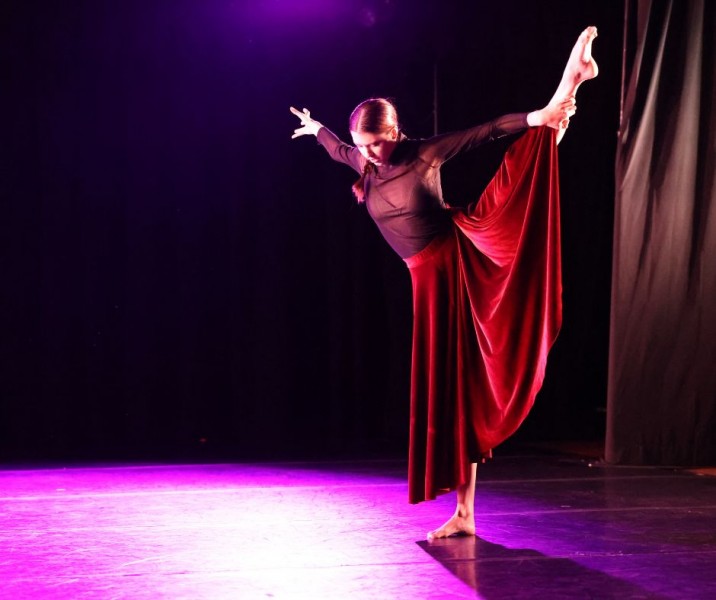 Dancer holding her left leg out to the side, wearing a black leotard and black long skirt.