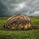 large rock in a grassy field, stormy sky above