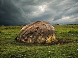 large rock in a grassy field, stormy sky above