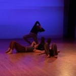 Three dancers lying on the ground connected while one dancer leans backwards on a medium level.