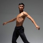 Company dancer stands in stoic pose against a greyscale backdrop.