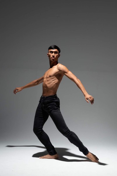 Company dancer stands in stoic pose against a greyscale backdrop.