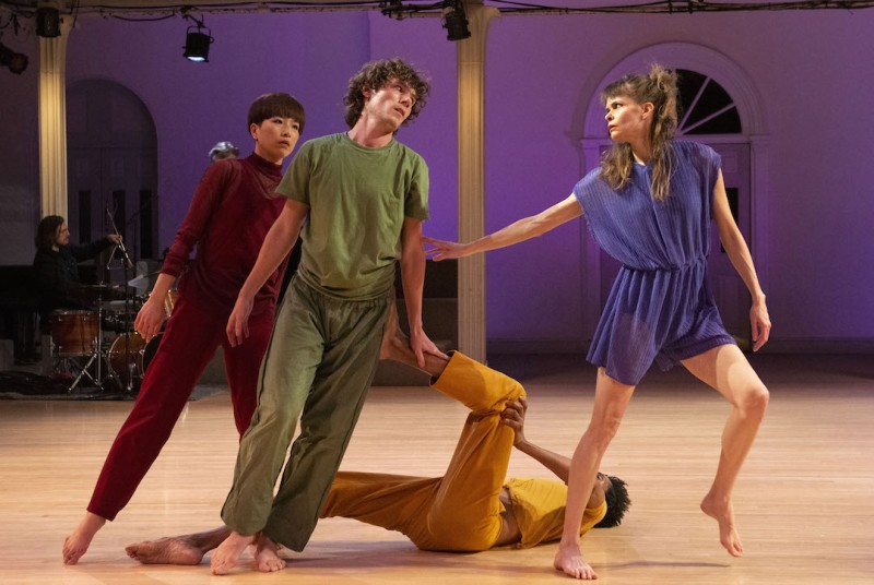 Four dancers on stage wearing red, green, yellow, and blue