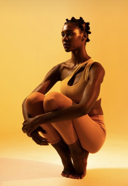 Dark skinned woman squatted wearing warm tone lathering wear with warm lighting resembling magic hour.