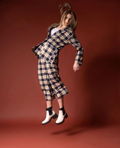 (Woman in plaid pant suit jumping in front of a red backdrop)