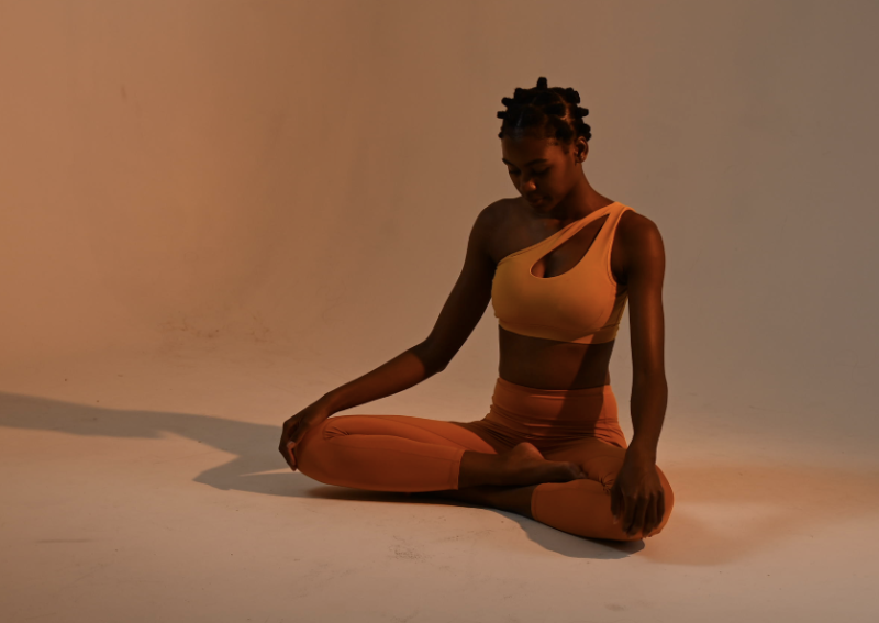 young black female yoga instructor sitting in a lotus pose wearing warm tone athletic wear