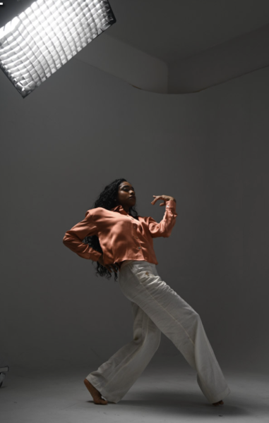 young lady moving wearing white pants and coral long sleeve shirt with lighting above 