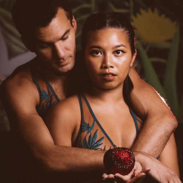 two actors, playing Adam and Eve, are holding a red, bedazzled apple.