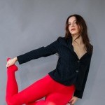 A dancer in red tights and black shirt poses on a stool in a studio