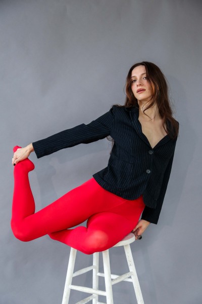 A dancer in red tights and black shirt poses on a stool in a studio