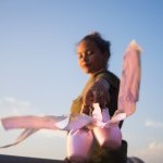 A ballerina holding her pointe shoes, with a soft focus on her hands and shoes, showcasing the elegance and precision of ballet