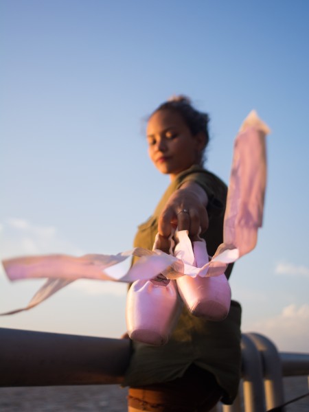 A ballerina holding her pointe shoes, with a soft focus on her hands and shoes, showcasing the elegance and precision of ballet