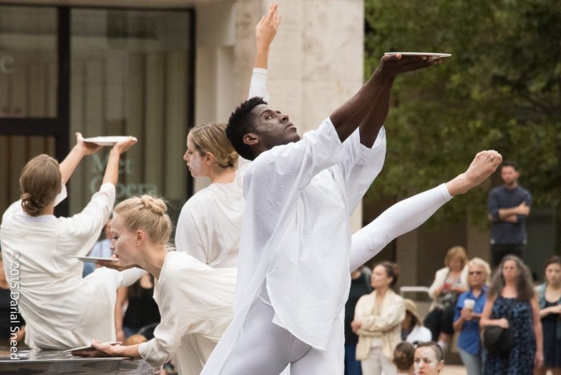 Dancers in white lifting a white ceramic plate to the sky 