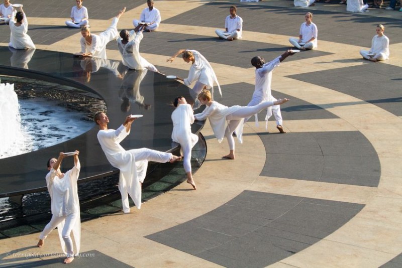multiple dancers in white around a circular black marble fountain