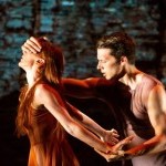 Male dancer with short light brown hair covering eyes of female dancer with long red hair 