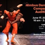 Male dancer in orange carries upside down female dancer in black with legs in split.