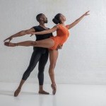 A pair of dancers stand in arabesque