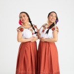 Two dancers pose together and wear red skirts and white shirts