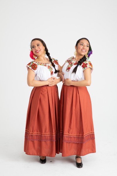 Two dancers pose together and wear red skirts and white shirts