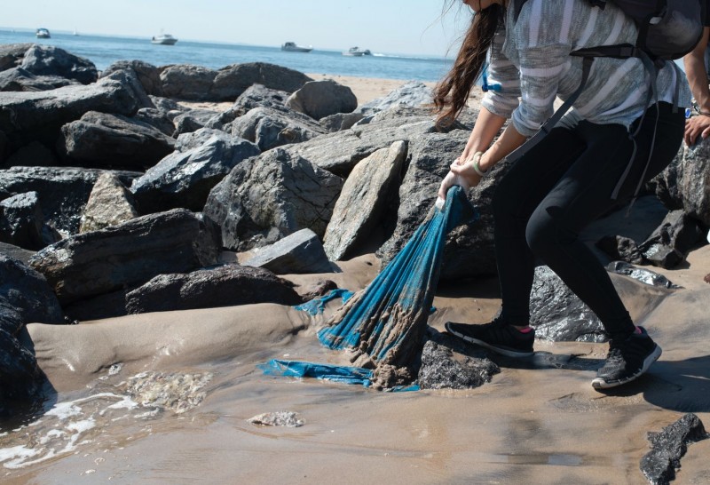 On the shore of Manhattan Beach a woman pulls out a blue fabric stuck under de sand and between the rocks. 