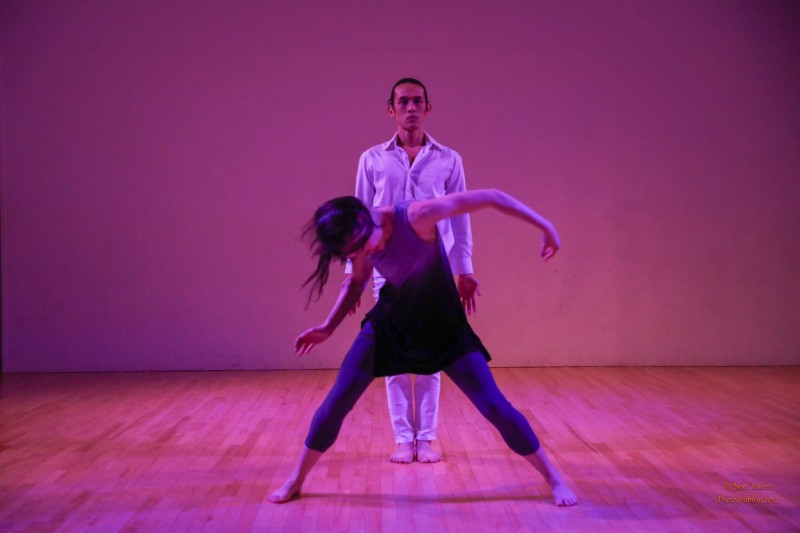dancer in front in blue and grey wide stance, pulling downward, dancer in white standing quietly behind her.