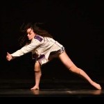 An image of a female dance on stage in a side lunge with arms clasped to the left