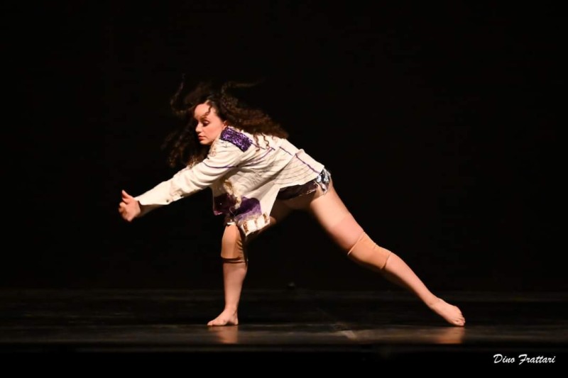 An image of a female dance on stage in a side lunge with arms clasped to the left