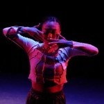 Dancer stands in red light with hands in front of face