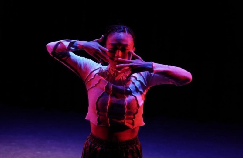 Dancer stands in red light with hands in front of face