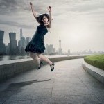 Dancer in black cocktail dress and heels jumping with hips forward, arms overhead, and legs back