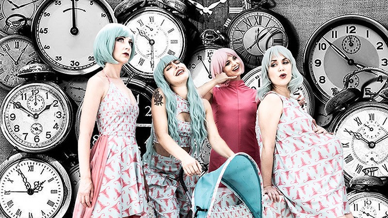 Four performers dressed in pink and green costumes infront of a background of black and white clocks.