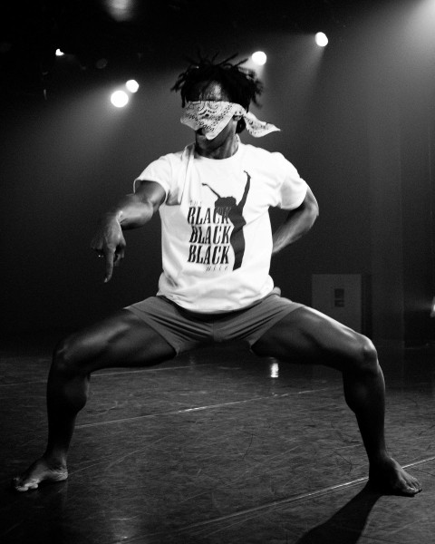 Image of Cemiyon Barber blindfolded with a bandana in second position pointing down and wearing a BBB Week t-shirt.