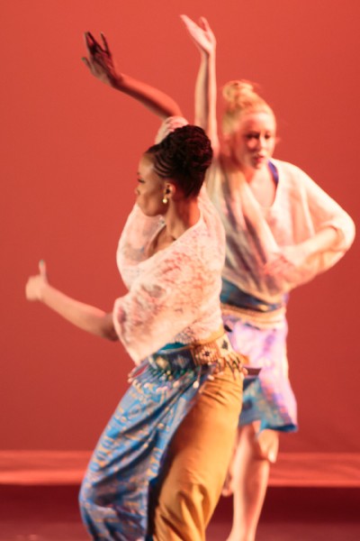 Two dancers in cream tops and blue and mustard skirts with orange background