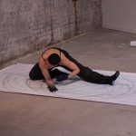 A dancer in black clothing dances on the floor on a large piece of paper.