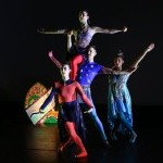 Multiple dancers in colorful costumes stacked next to sculpture