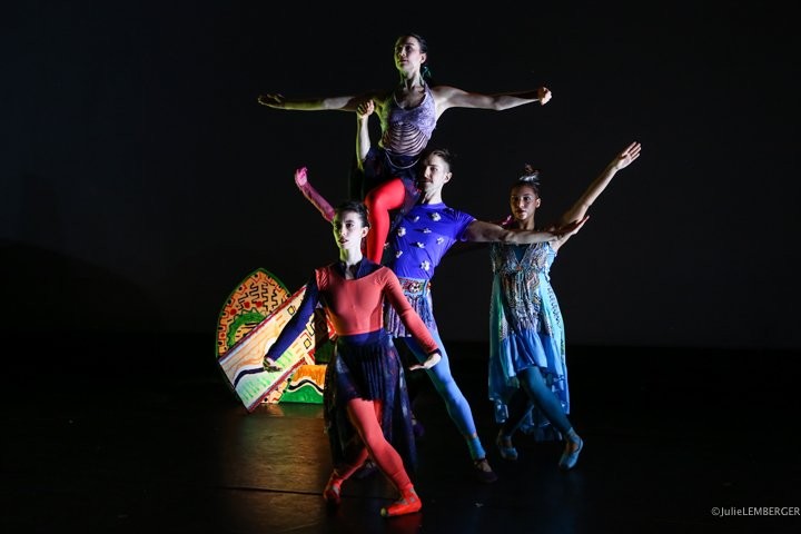 Multiple dancers in colorful costumes stacked next to sculpture