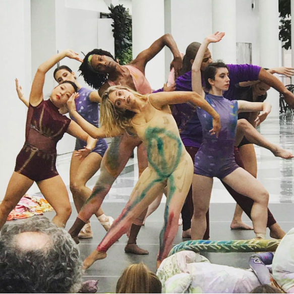 Group of dancers in multicolor unitards arching and tipping.