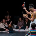 Performer holding a bird puppet and nest looking down at a small child from the audience