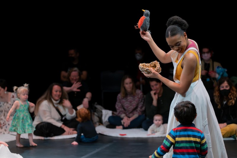 Performer holding a bird puppet and nest looking down at a small child from the audience