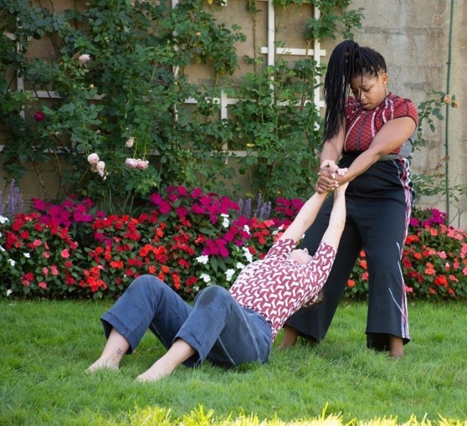 Two dancers connected at the hands dancing in grass in front of flowers