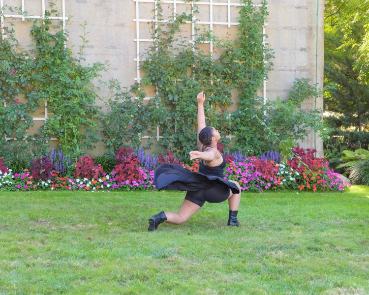 Dancer in a lunge dressed in black in front of a floral backdrop