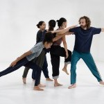 Five dancers are close together creating a cluster in a white dance studio.