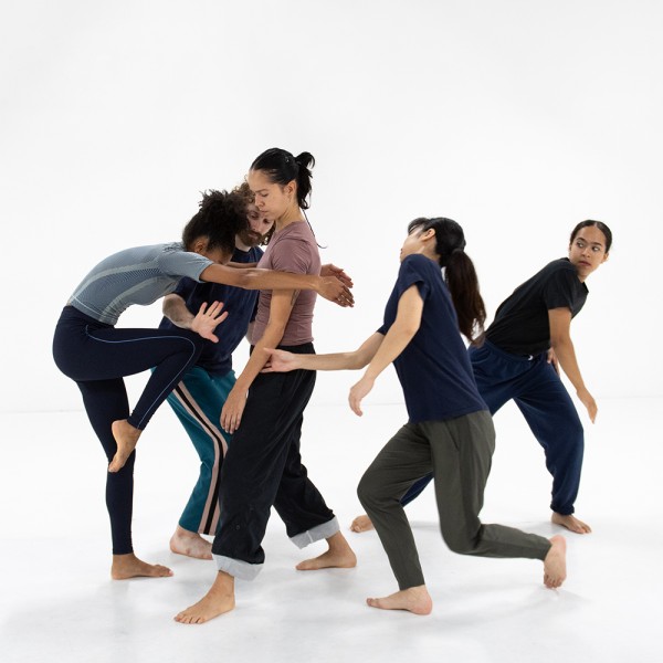 Five dancers are closely moving together in white dance studio.