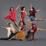 Six dancers with color outfits against a plain grey background