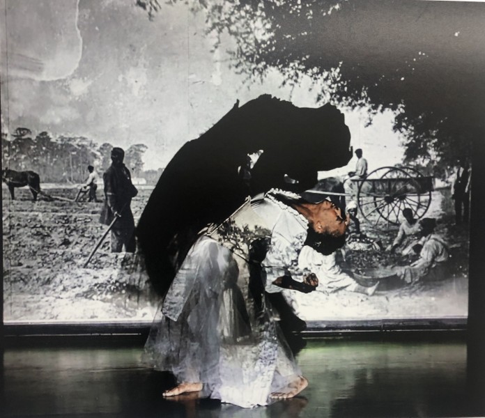 Image of a brown woman dressed in civil war era attire arched while dancing in front of a projection of a B&W vintage photograph